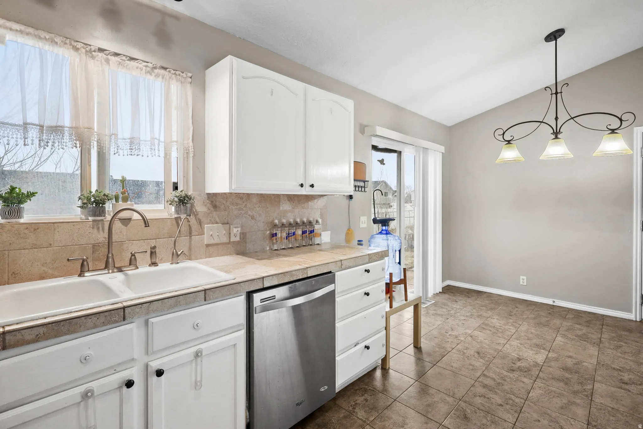 Kitchen with white cabinets, dishwasher, decorative backsplash, vaulted ceiling, and hanging light fixtures