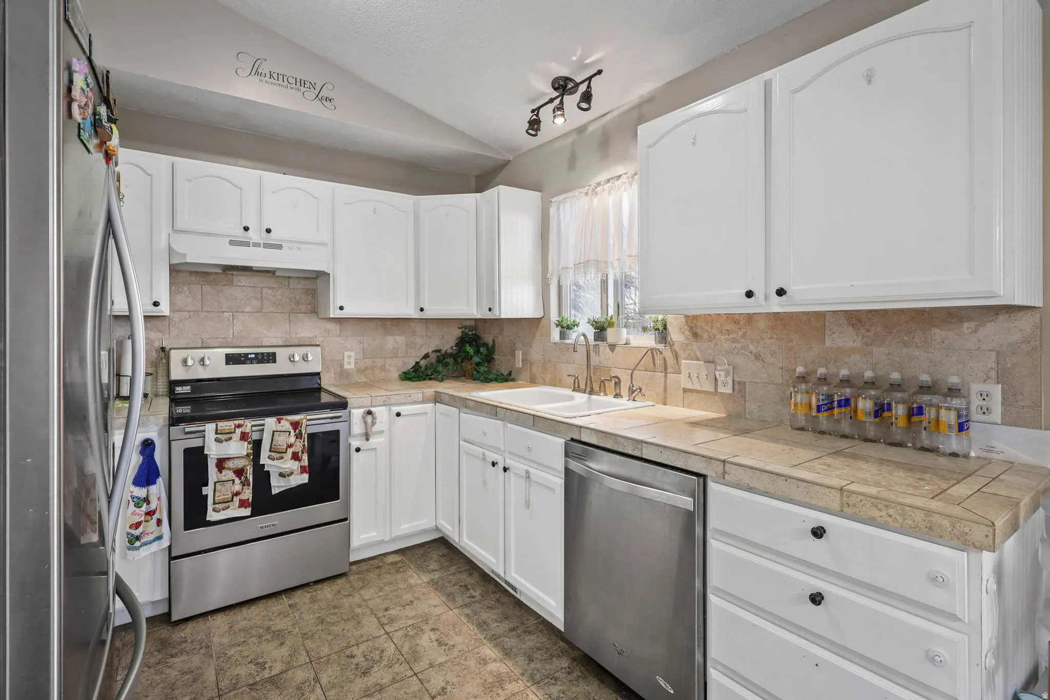 Kitchen with lofted ceiling, stainless steel appliances, white cabinetry, and backsplash