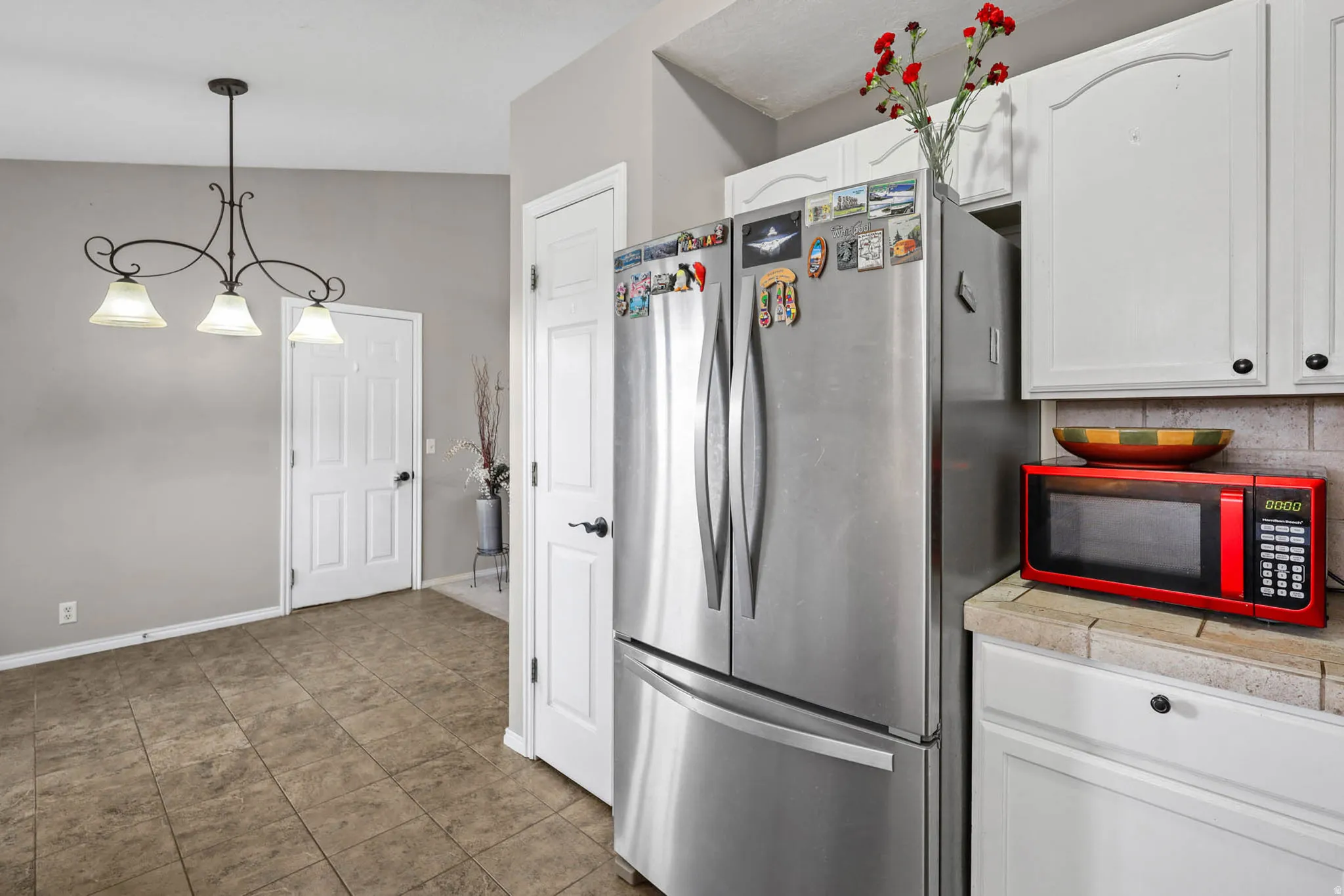 Kitchen featuring freestanding refrigerator, white cabinetry, and decorative light fixtures