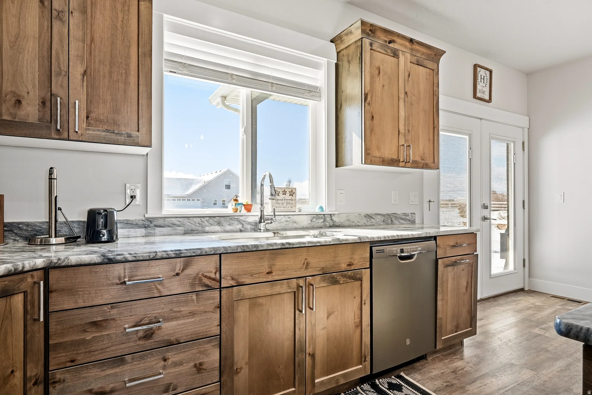Kitchen featuring stainless steel dishwasher, dark wood finished floors, light stone countertops, and healthy amount of natural light