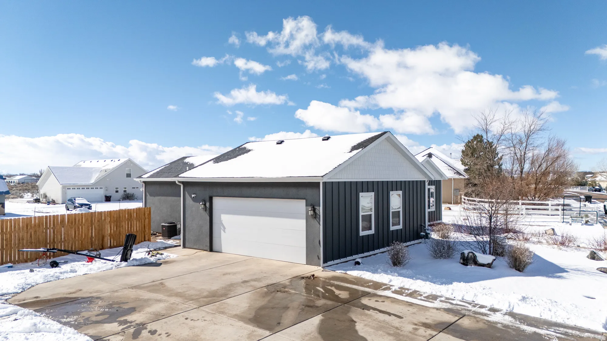 View of snow covered exterior with a garage, driveway, and board and batten siding