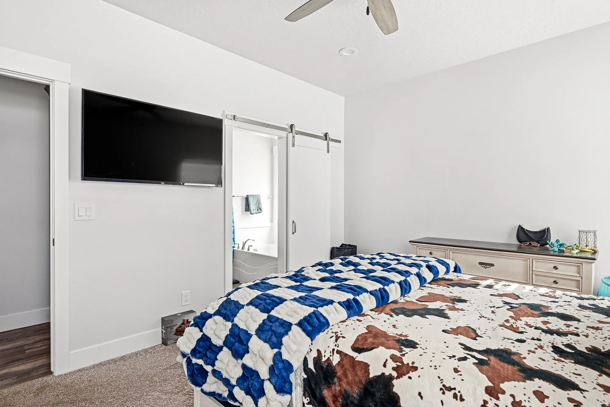 Bedroom with a barn door, ensuite bathroom, carpet flooring, and ceiling fan