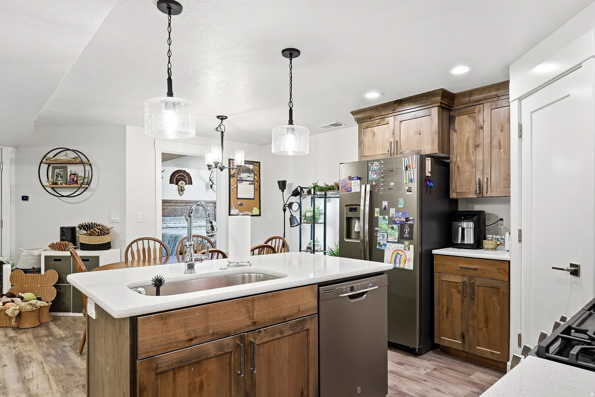 Kitchen with decorative light fixtures, stainless steel appliances, a kitchen island with sink, and light stone countertops