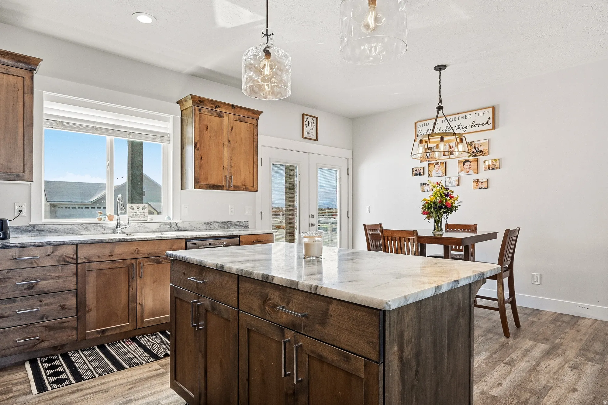 Kitchen with a kitchen island, decorative light fixtures, light wood-type flooring, and light stone countertops