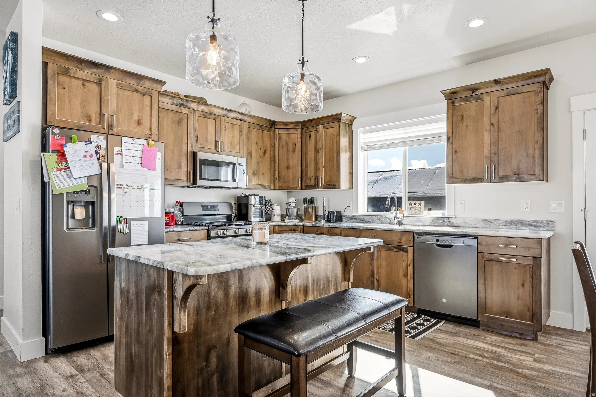 Kitchen featuring decorative light fixtures, stainless steel appliances, a kitchen island, a kitchen breakfast bar, and light stone countertops