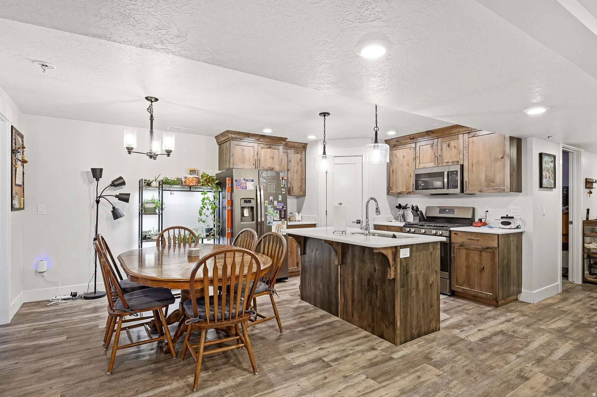 Kitchen with stainless steel appliances, light wood-type flooring, a textured ceiling, a breakfast bar area, and a center island with sink