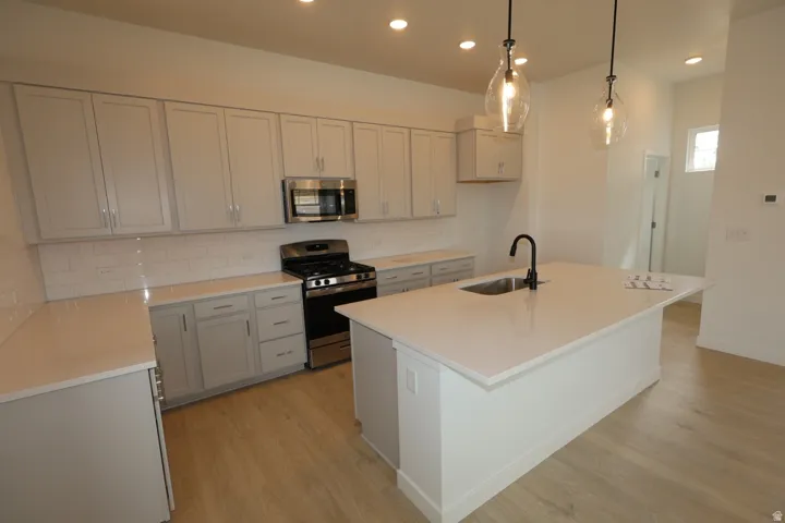 Kitchen featuring stainless steel appliances, tasteful backsplash, a center island with sink, light wood-style flooring, and decorative light fixtures