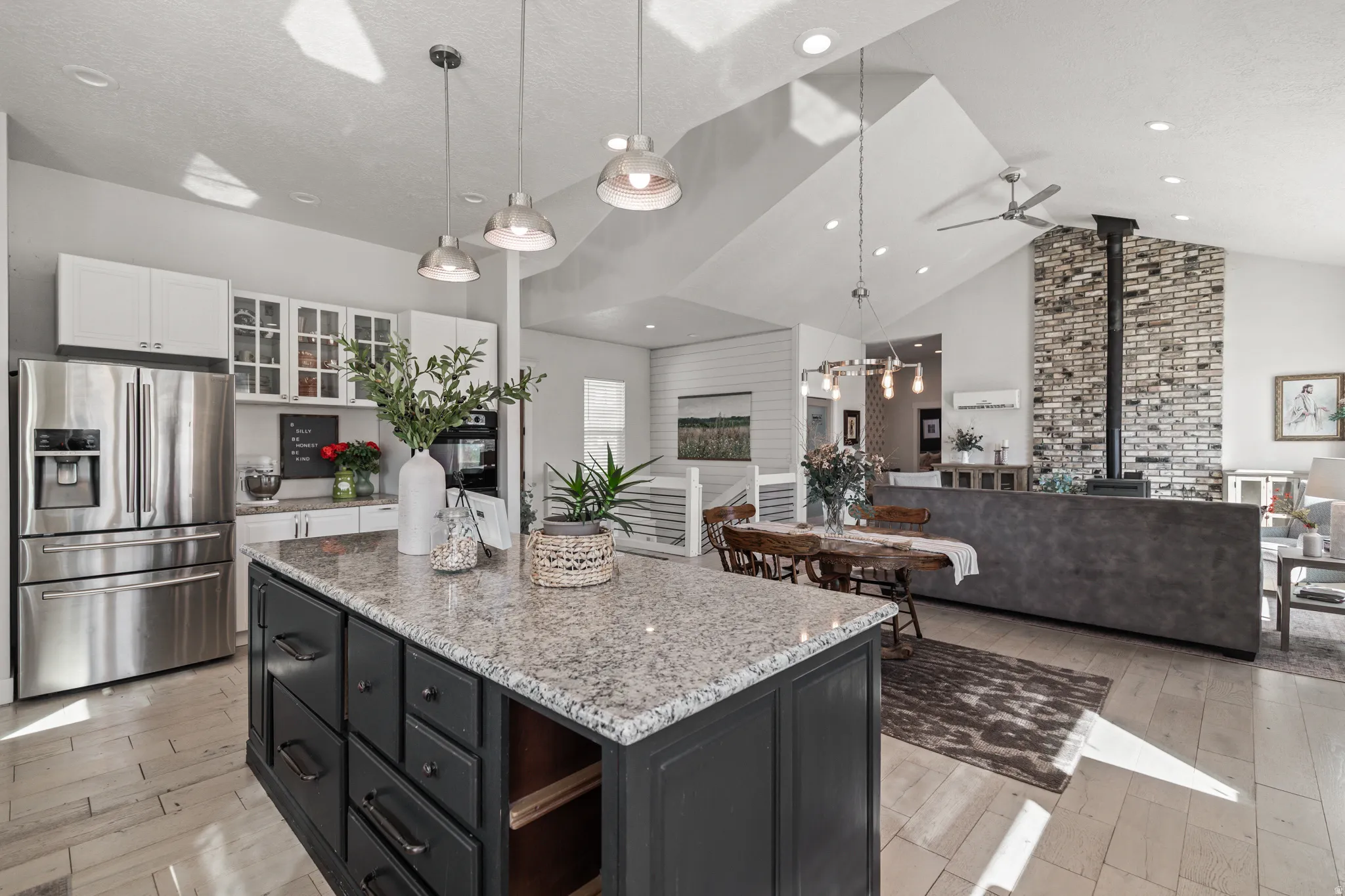 Kitchen with stainless steel fridge with ice dispenser, light stone counters, a wood stove, glass fronted cabinets, and a high ceiling