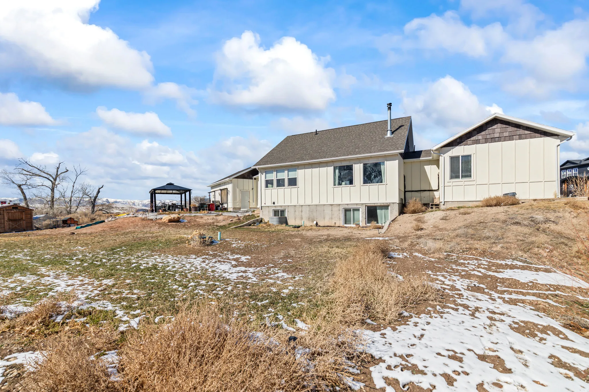 Snow covered property featuring board and batten siding, a gazebo, and a shingled roof