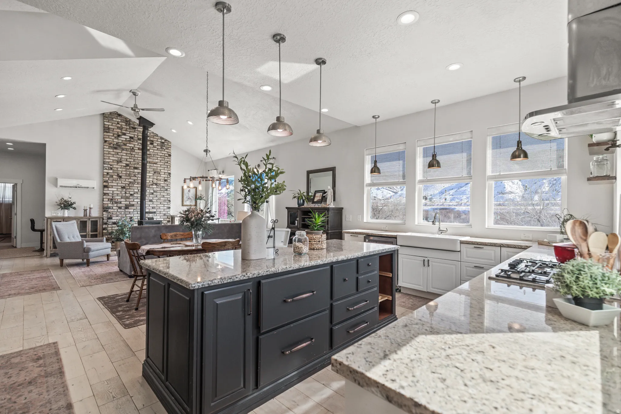 Kitchen with light stone counters, two tone cabinetry, range hood, pendant lighting, and a kitchen island