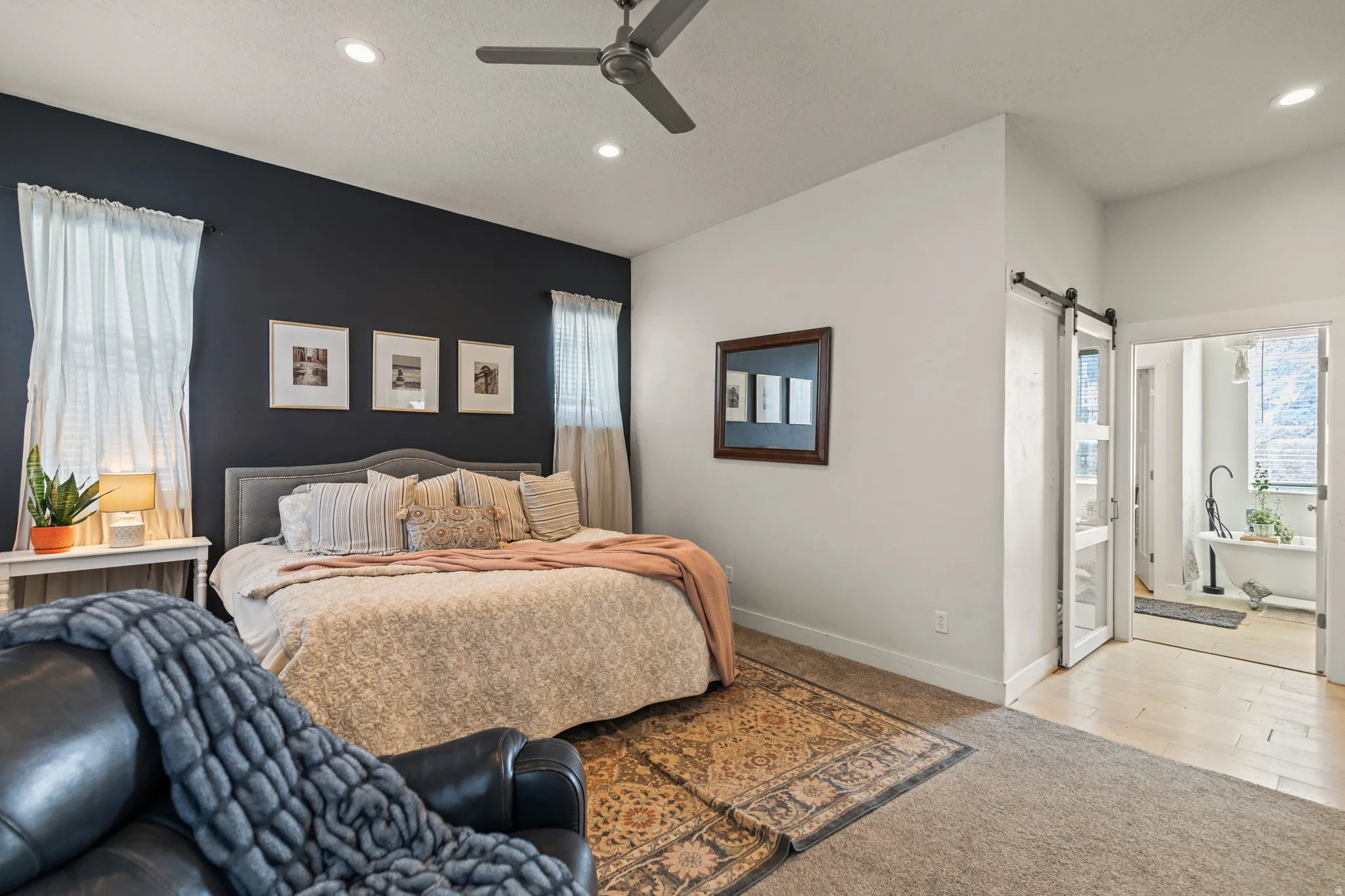 Carpeted bedroom with a barn door, multiple windows, a ceiling fan, recessed lighting, and ensuite bath