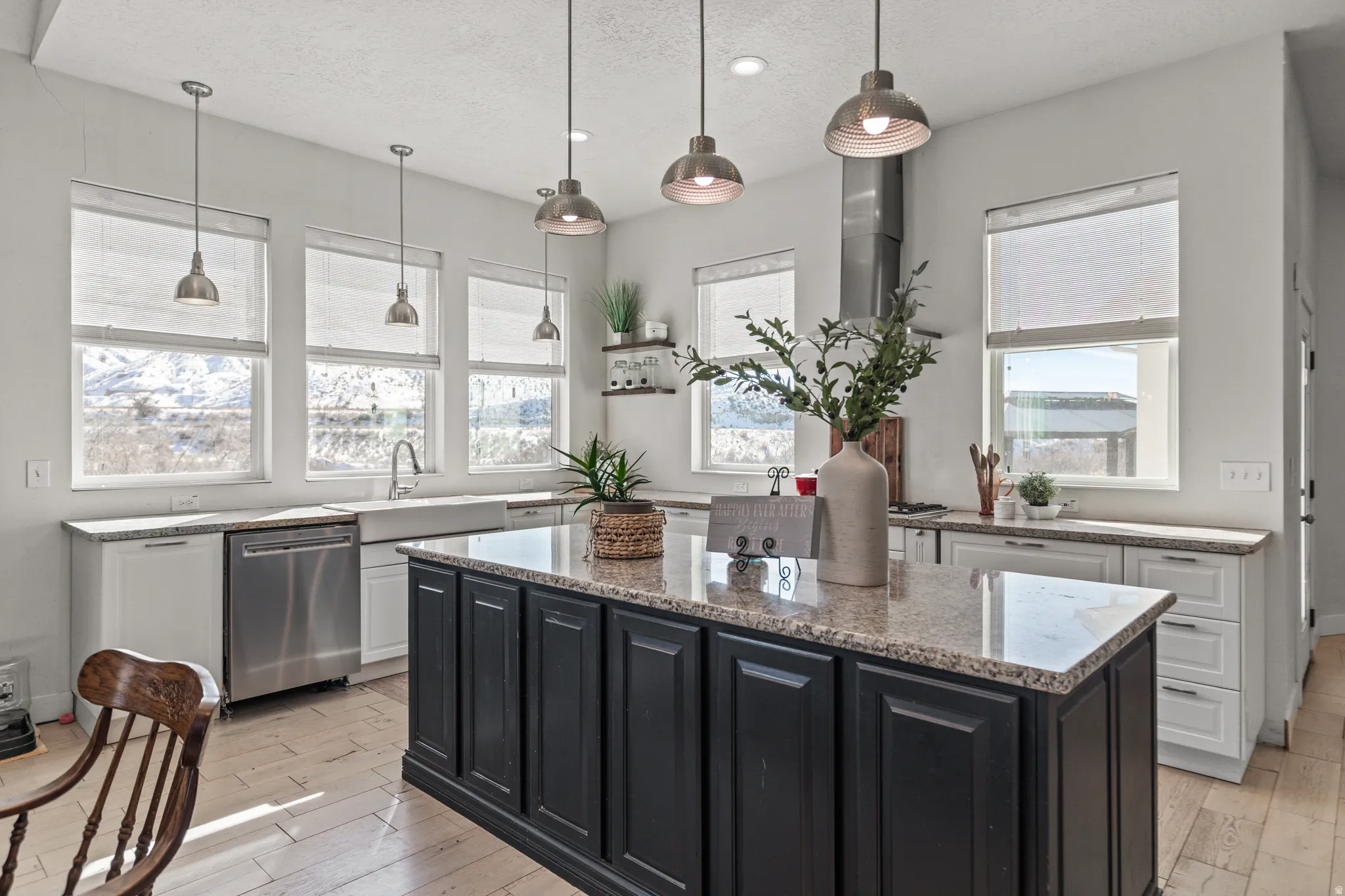 Two tone kitchen with light stone counters, stainless steel dishwasher, a kitchen island, pendant lighting, and light wood finished floors