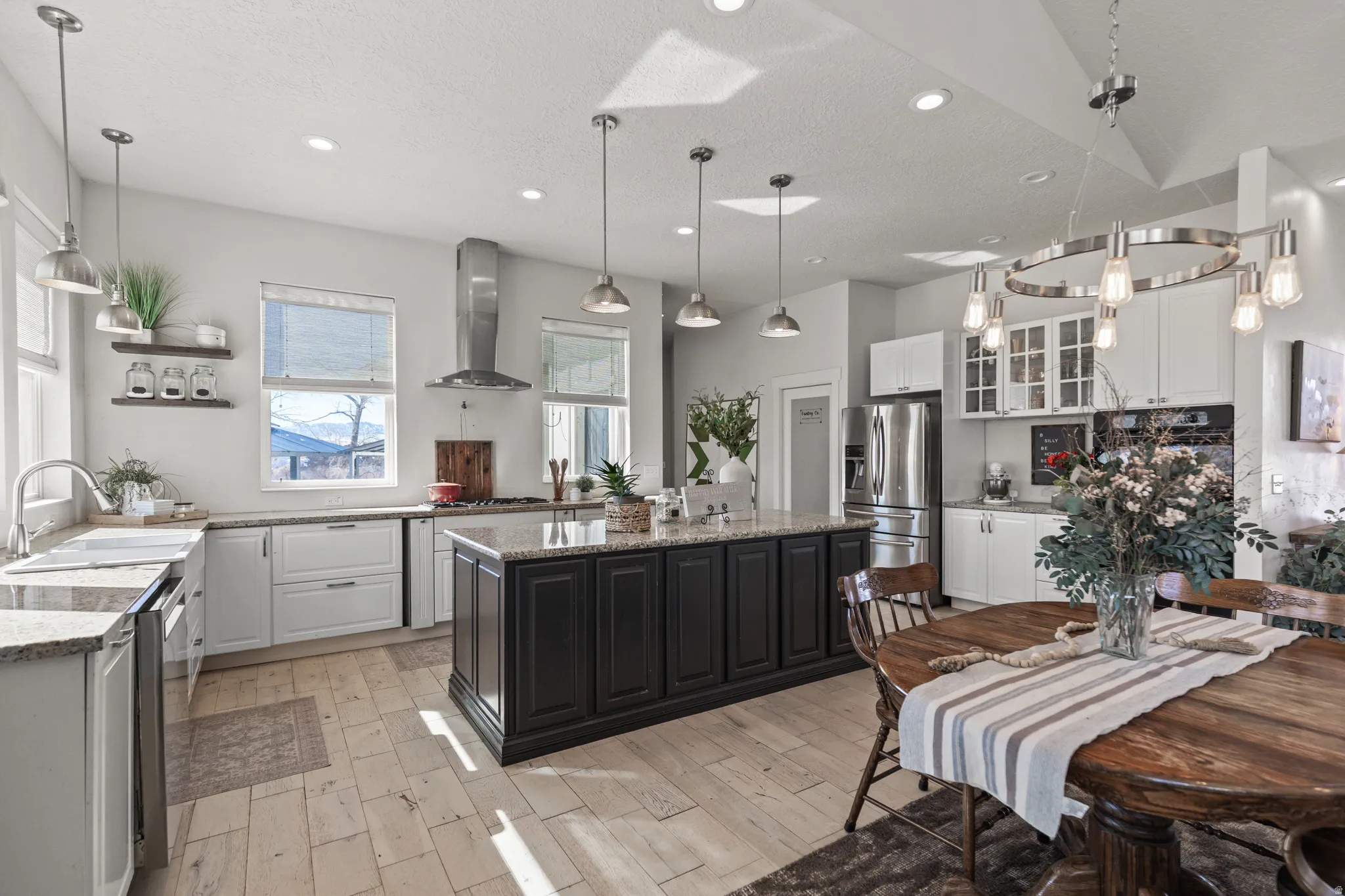 Two tone kitchen with glass fronted cabinets, light stone counters, hanging light fixtures, stainless steel appliances, and a center island