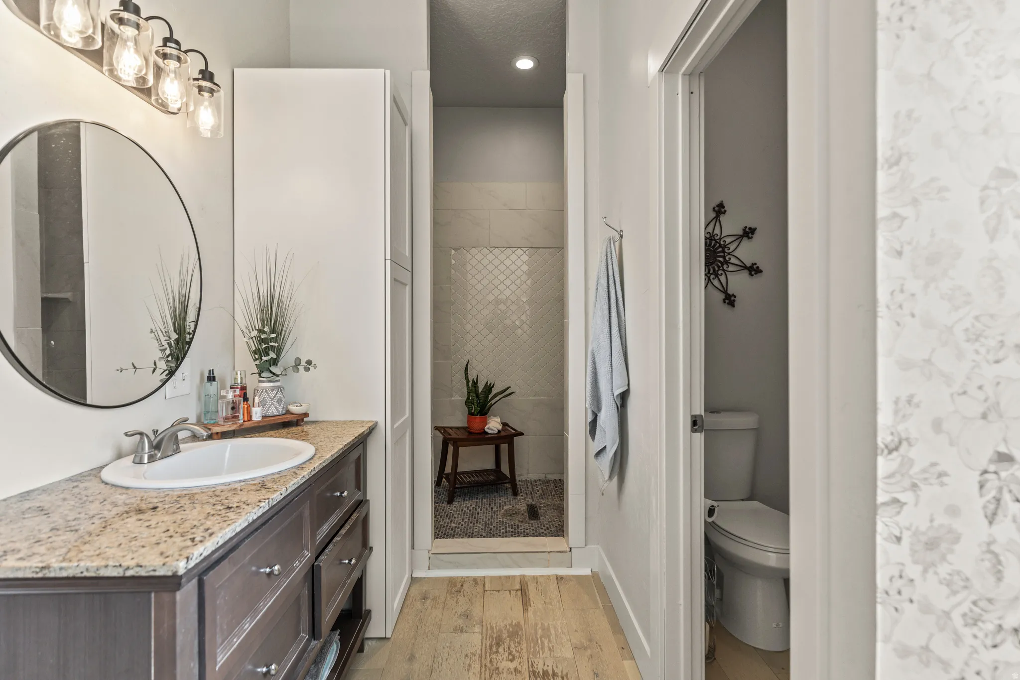 Bathroom featuring tiled shower, vanity, light wood-style floors, and recessed lighting