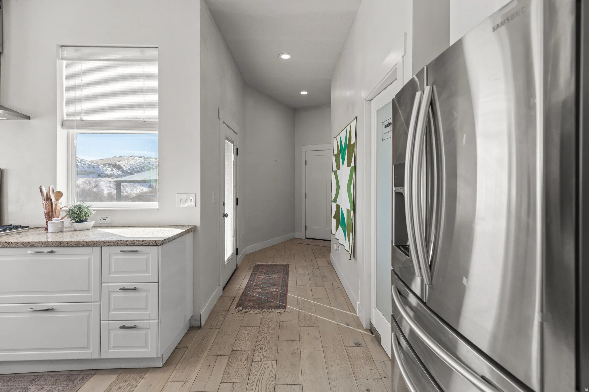 Kitchen with stainless steel fridge, white cabinets, light wood-type flooring, light stone countertops, and recessed lighting