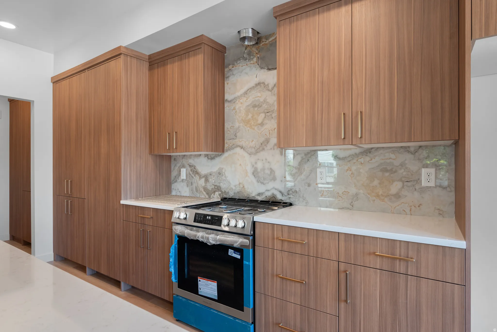 Kitchen featuring wood-finish cabinetry with brushed gold hardware, white countertops, and a patterned stone backsplash