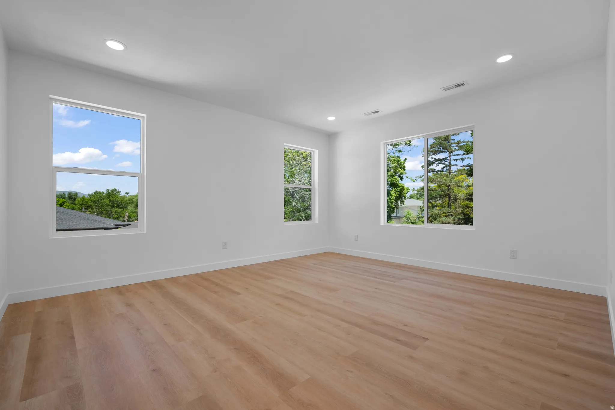 Spacious room featuring light wood-finish flooring, recessed lighting, and multiple windows