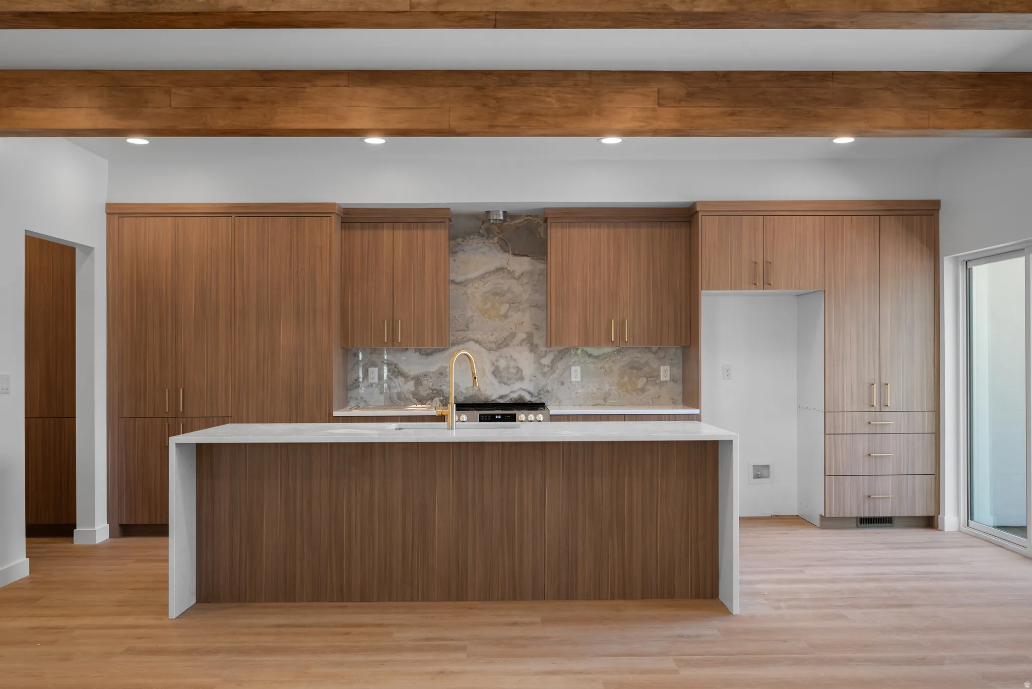 Modern kitchen featuring a large waterfall island with integrated sink, gold-finish faucet, and light-toned countertop