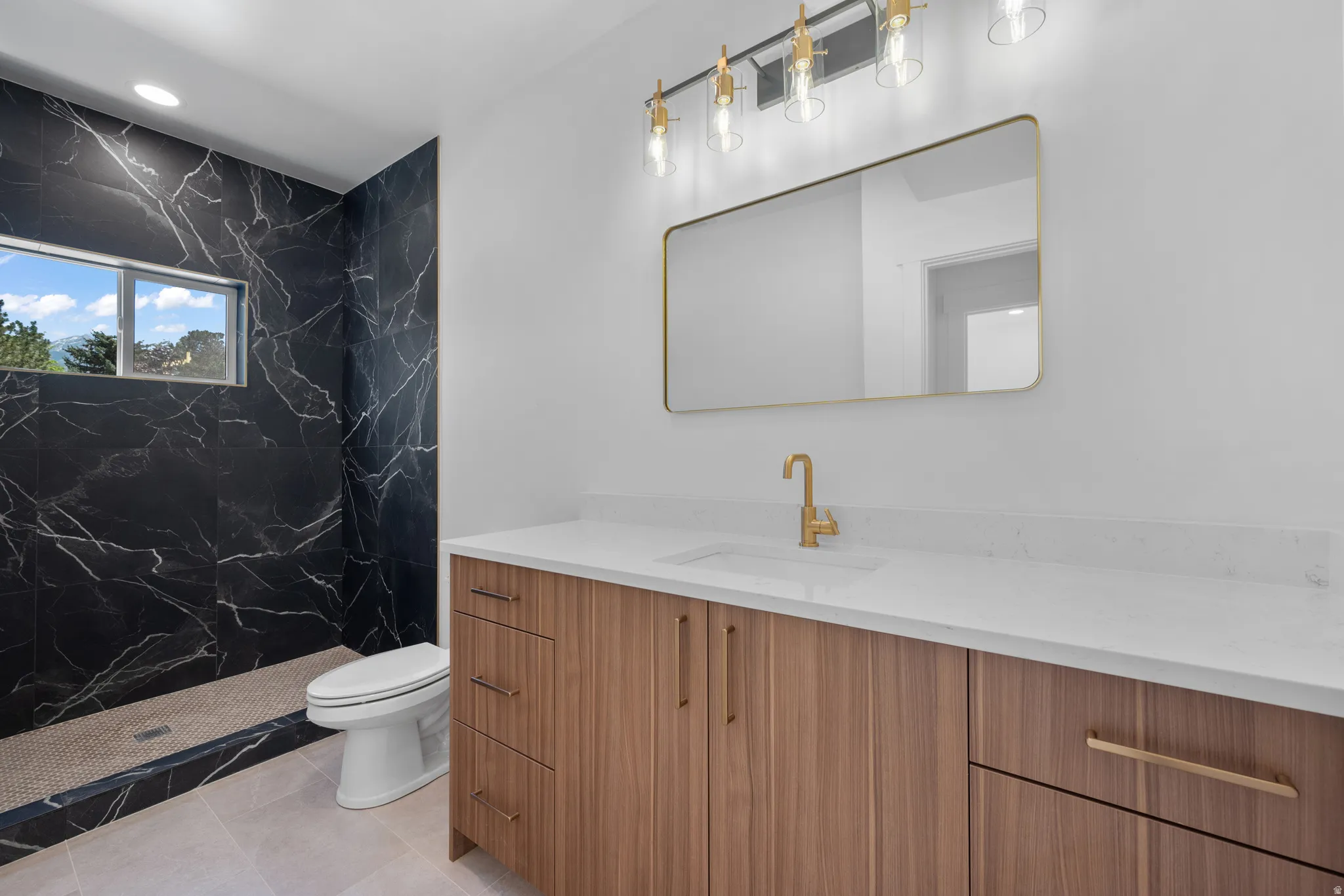 Modern bathroom featuring a wood-finish vanity with a white countertop and gold-tone fixtures