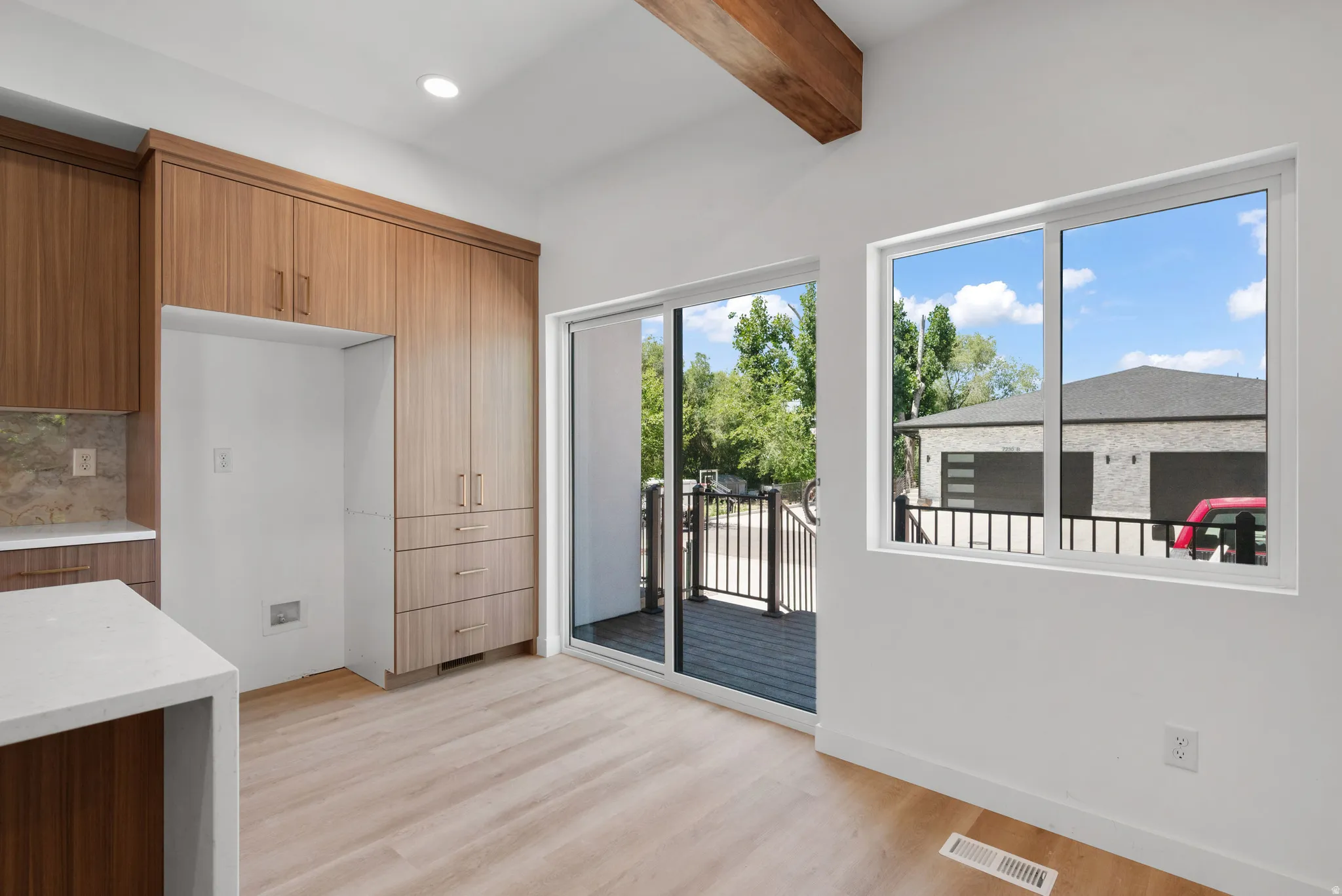 Open-concept living space with wood-finish flooring, a wood beam ceiling accent, and white walls