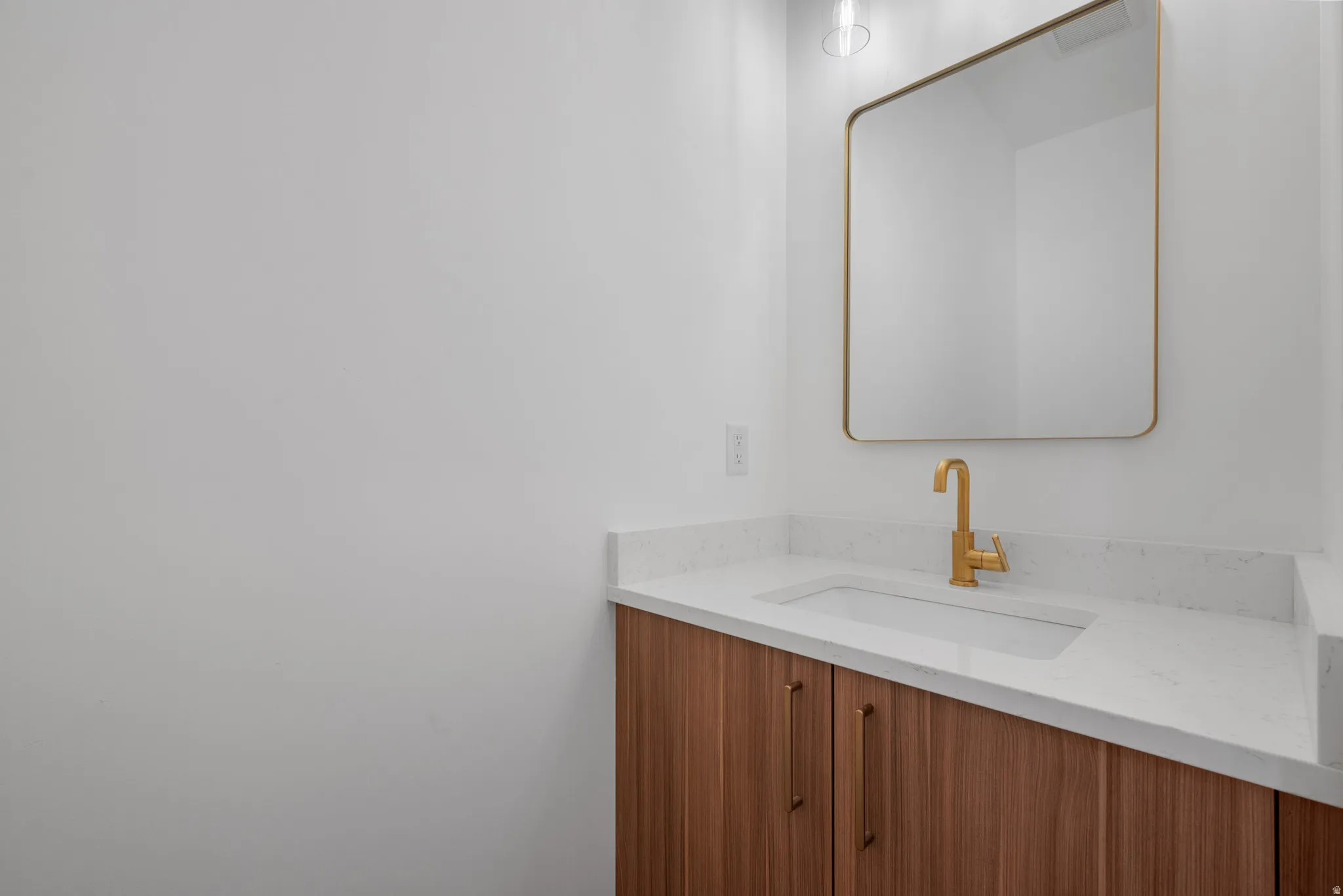Vanity featuring a wood-finish cabinet, gold-finish hardware, and a white countertop with an integrated rectangular sink