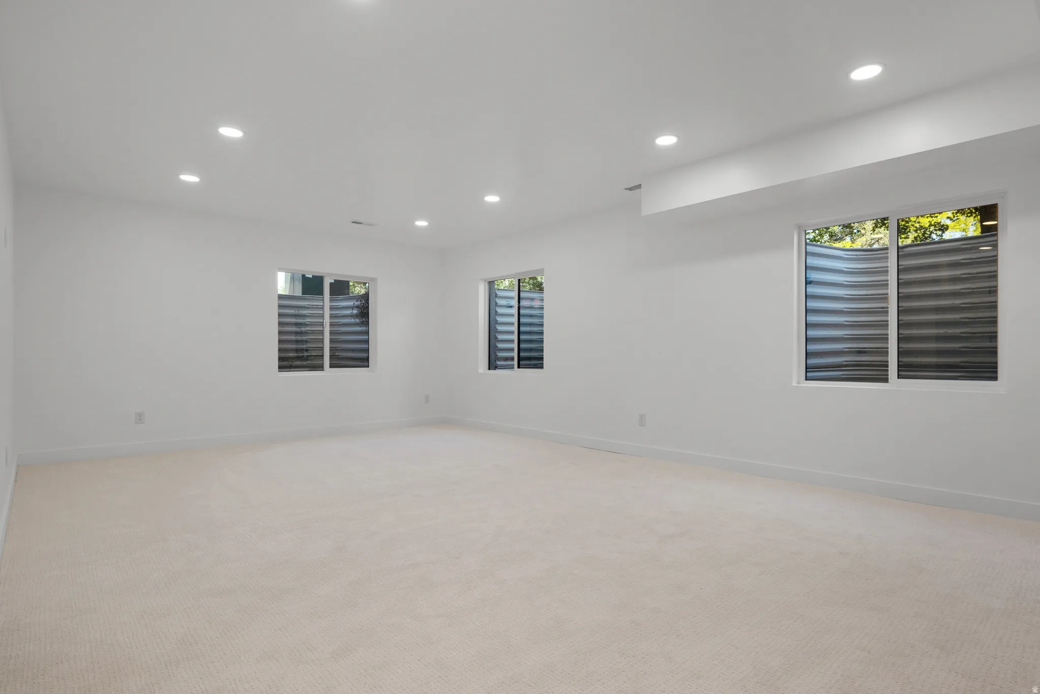 Spacious room featuring light-colored carpeting, multiple recessed lighting fixtures, and three large windows