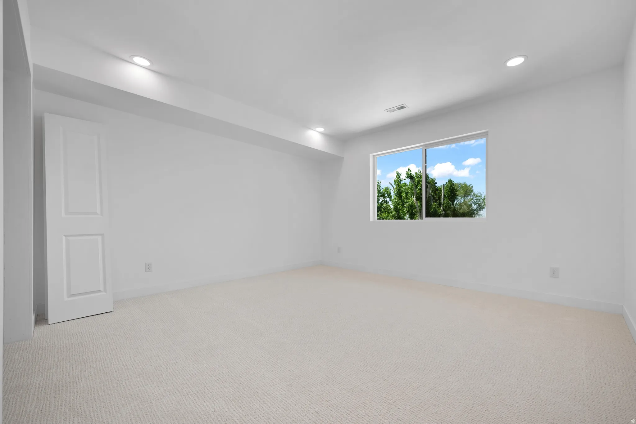 Bright room featuring a large window, plush carpet flooring, recessed lighting, and a paneled door