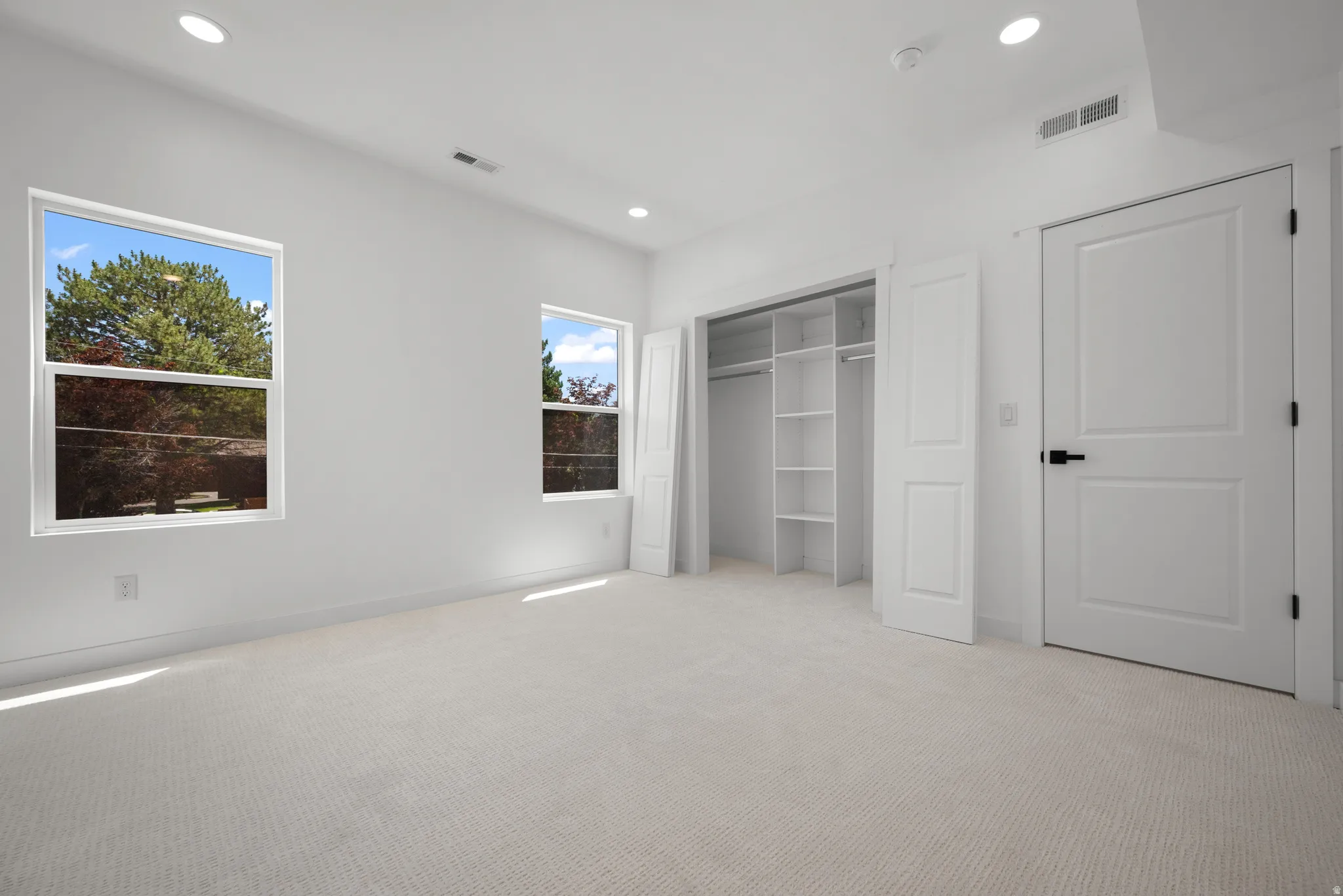 Light-toned carpeting in a room featuring two windows with exterior views, recessed ceiling lighting, and a built-in closet system with shelving and hanging rods