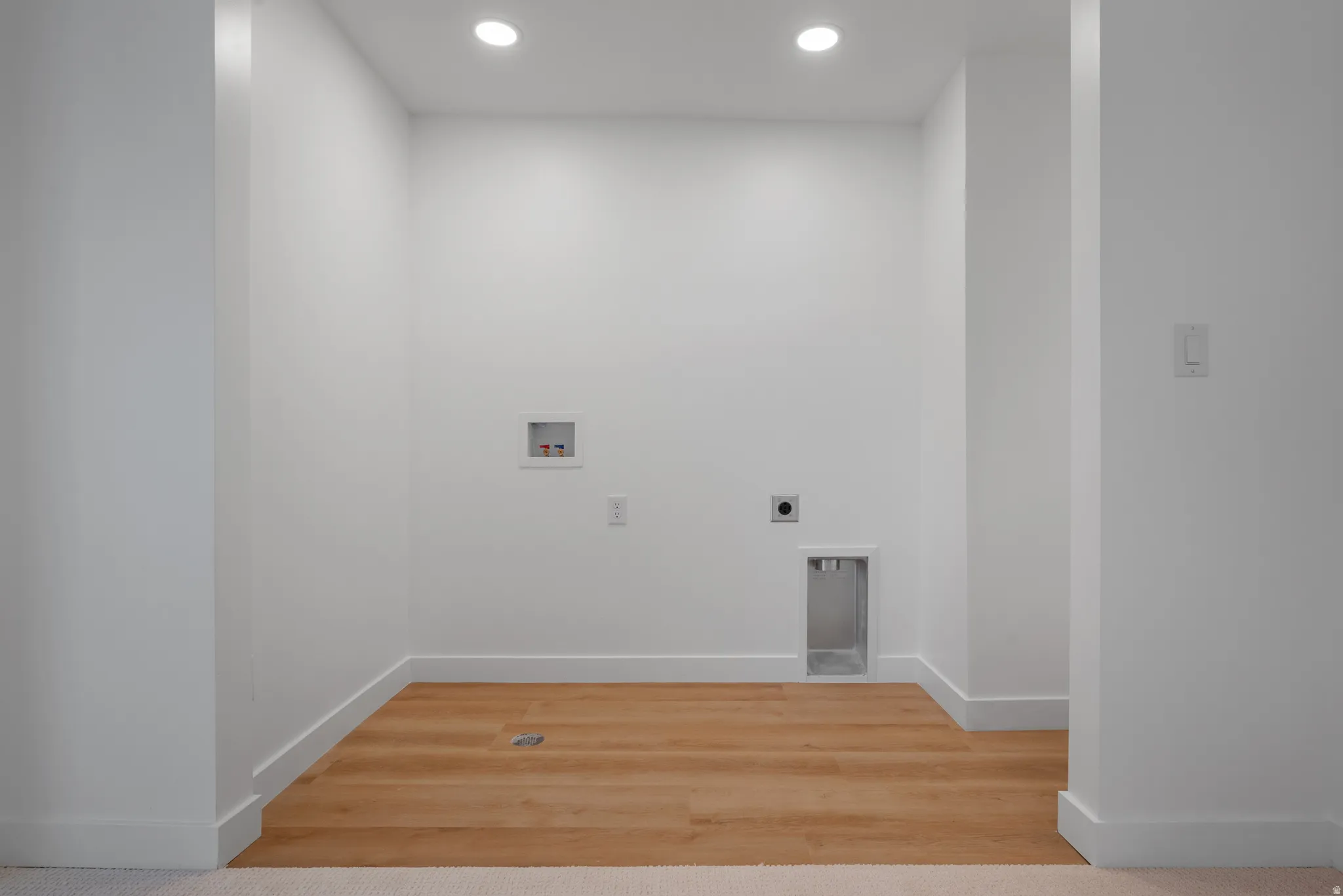 Dedicated utility space featuring bright recessed lighting and wood-finish flooring