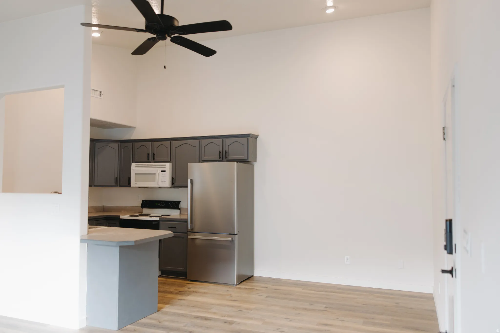 Kitchen featuring freestanding refrigerator, a high ceiling, light countertops, white microwave, and light wood-type flooring