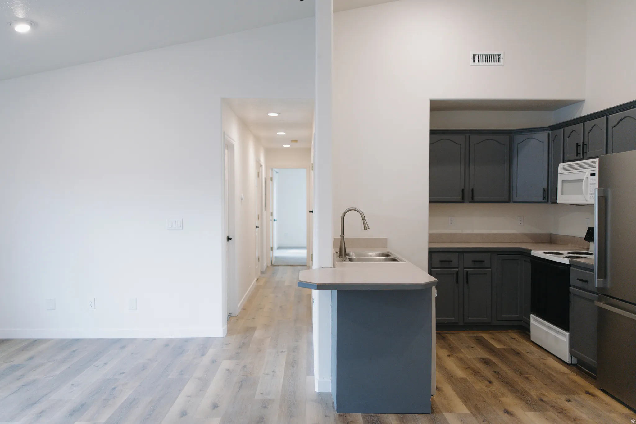 Kitchen with light countertops, range with electric stovetop, freestanding refrigerator, a peninsula, and recessed lighting