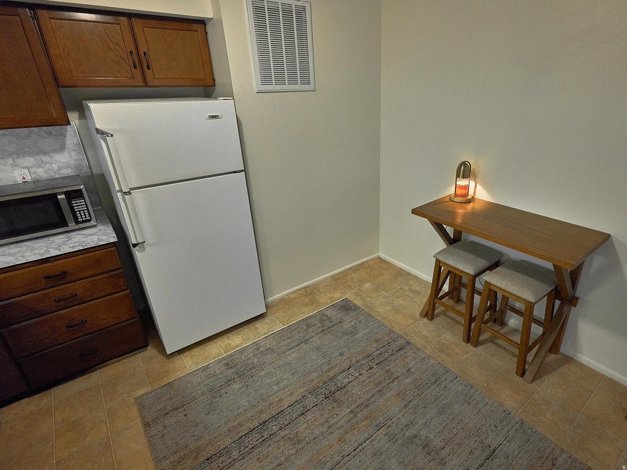 Kitchen with freestanding refrigerator, light countertops, stainless steel microwave, and wood finish cabinetry