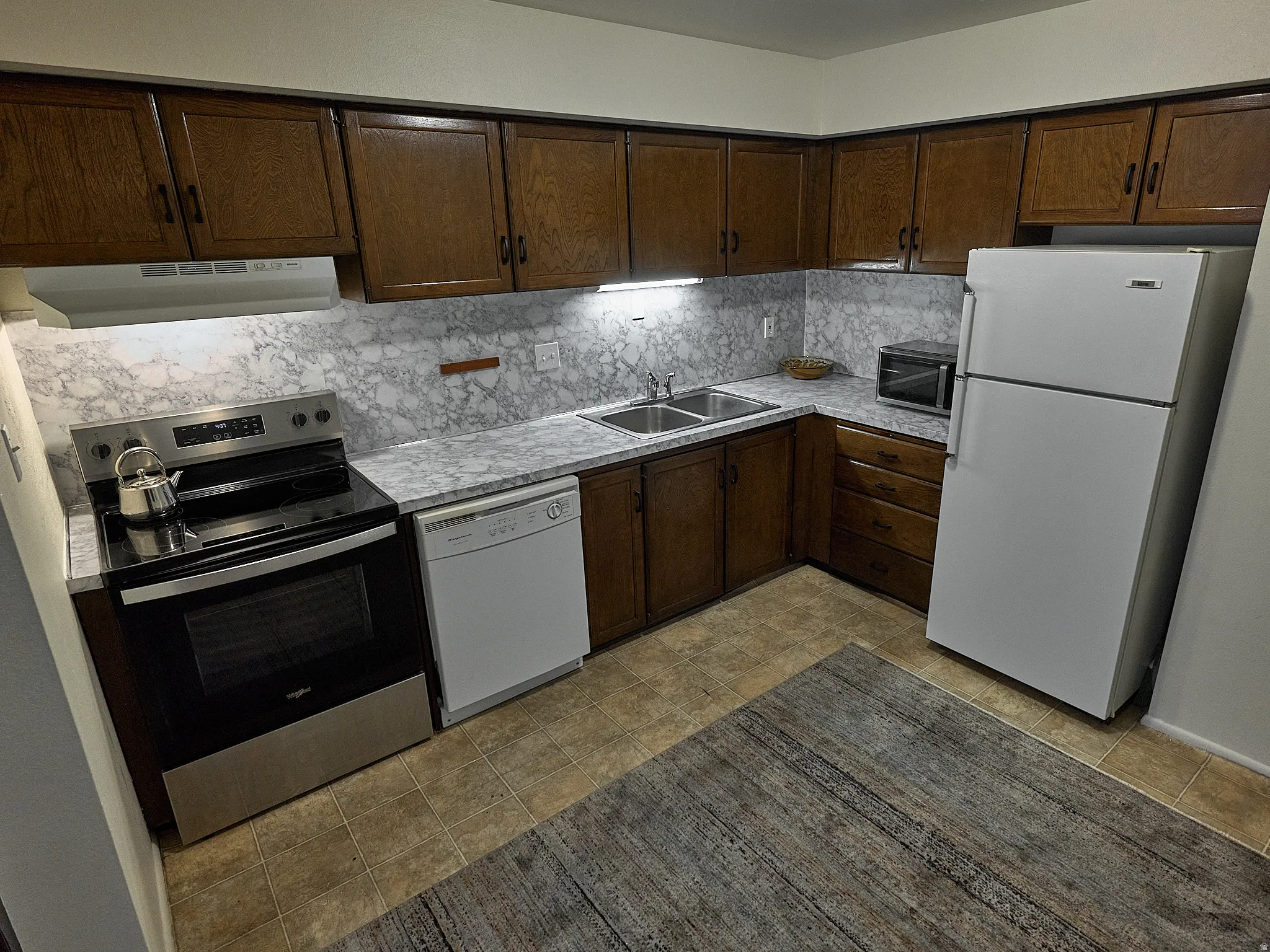 Kitchen featuring stainless steel appliances, dark wood finish cabinets, light countertops, and tasteful backsplash