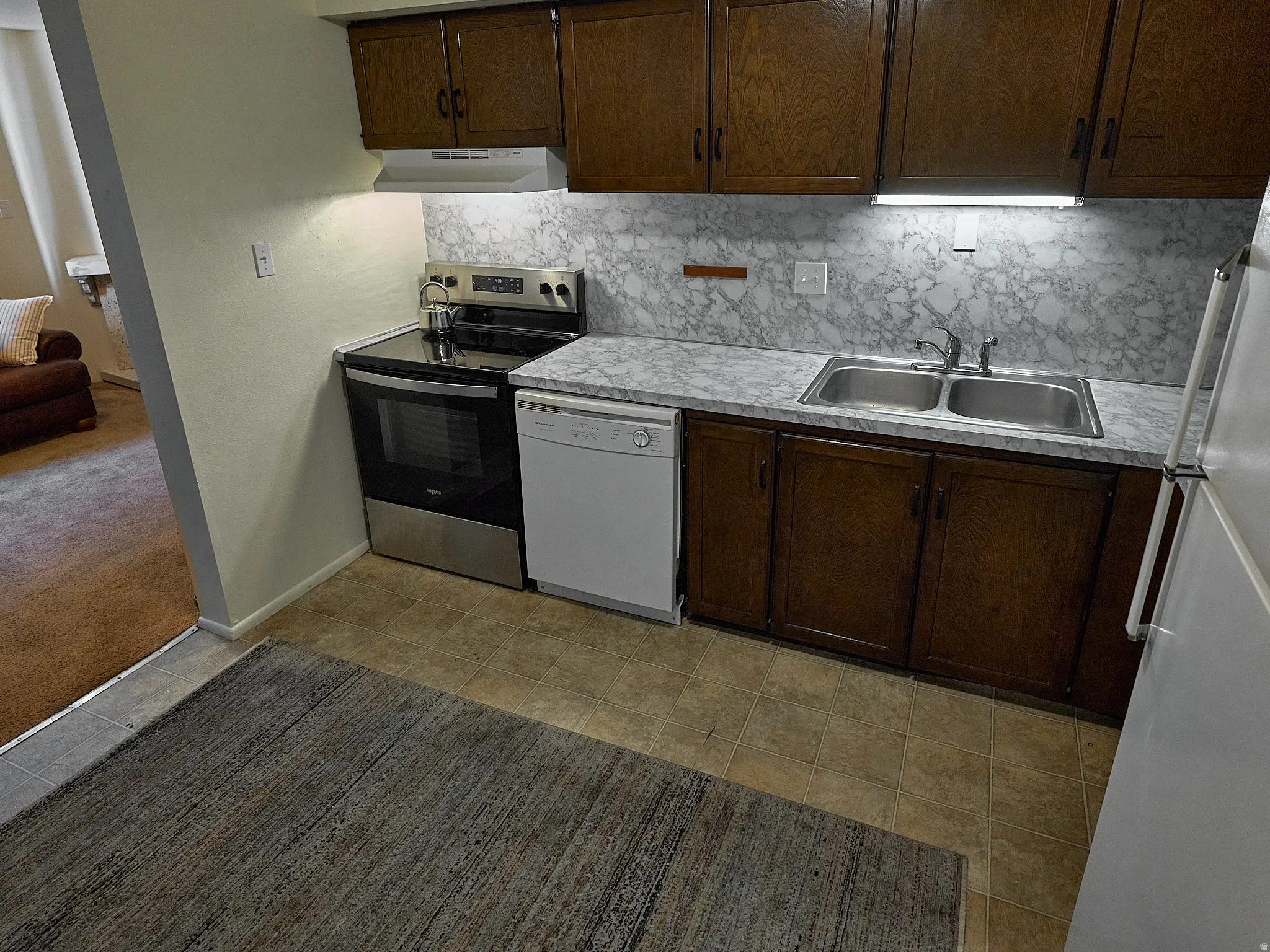 Kitchen featuring white appliances, light countertops, backsplash, and dark wood finish cabinets