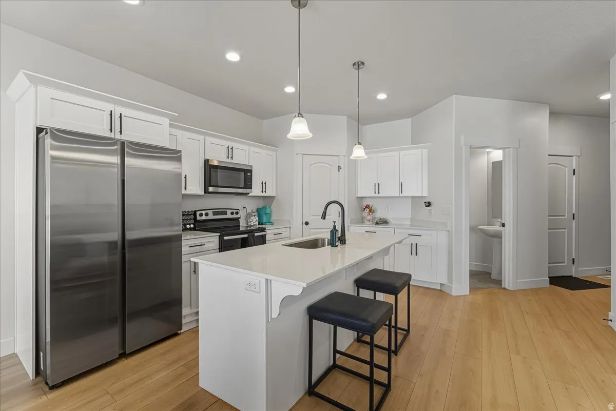 Kitchen with stainless steel appliances, a kitchen bar, white cabinets, and light wood-type flooring