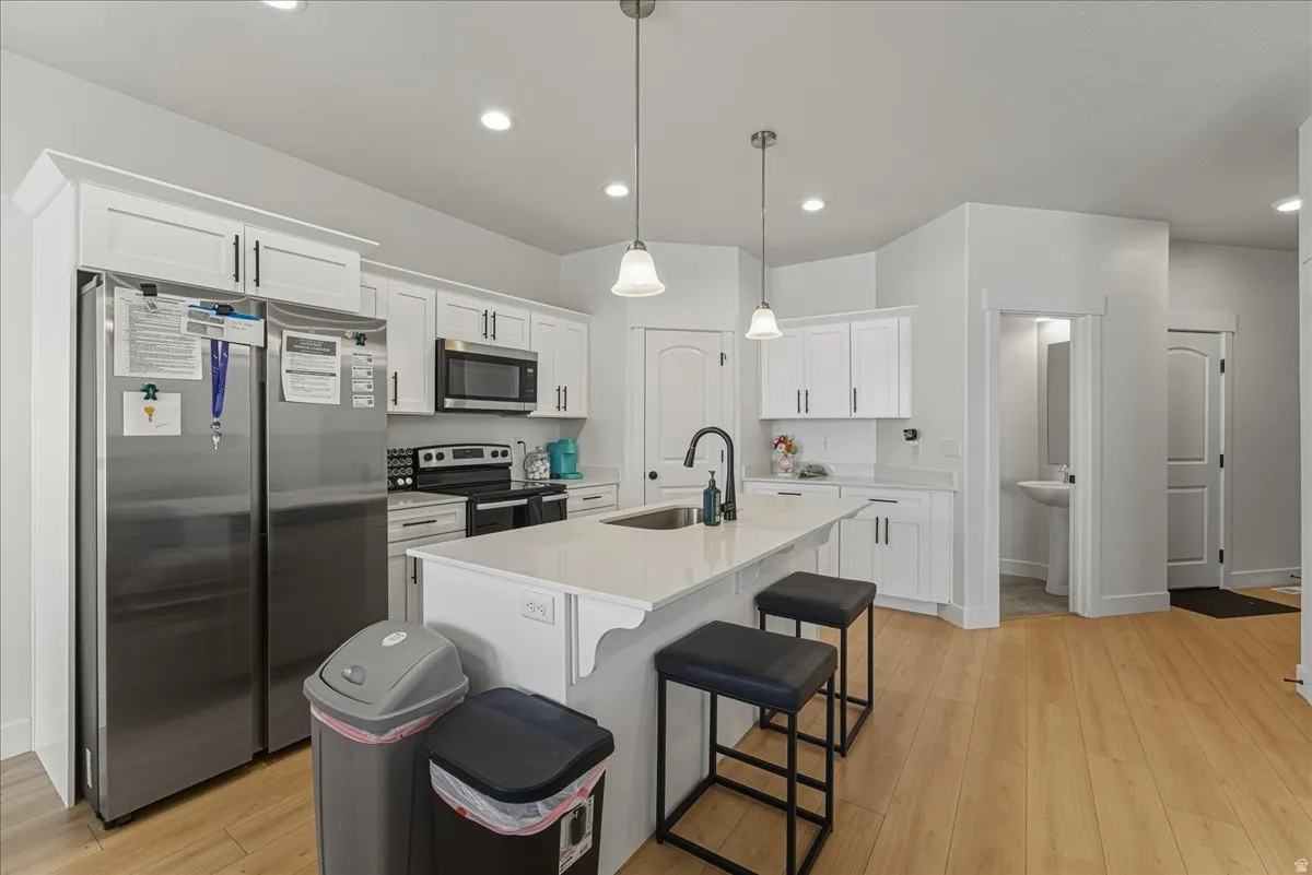 Kitchen with stainless steel appliances, white cabinetry, a breakfast bar area, and light wood-type flooring