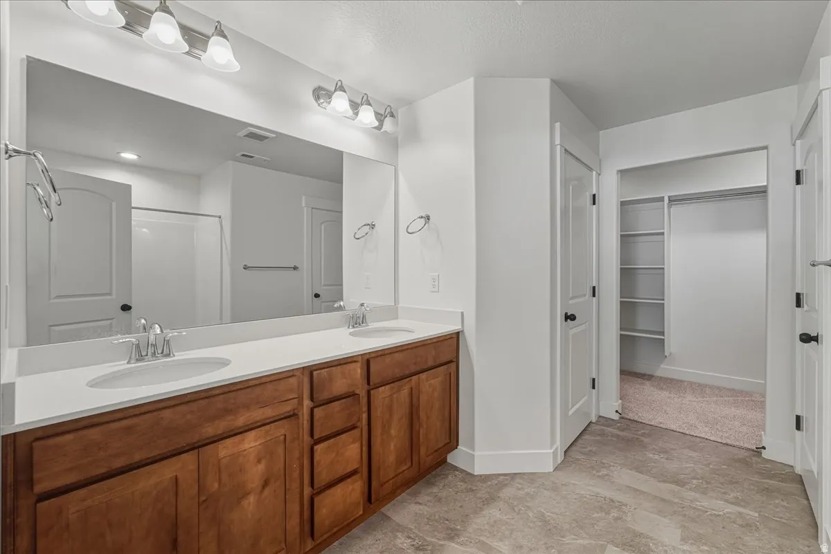 Full bathroom featuring a spacious closet, double vanity, and a shower