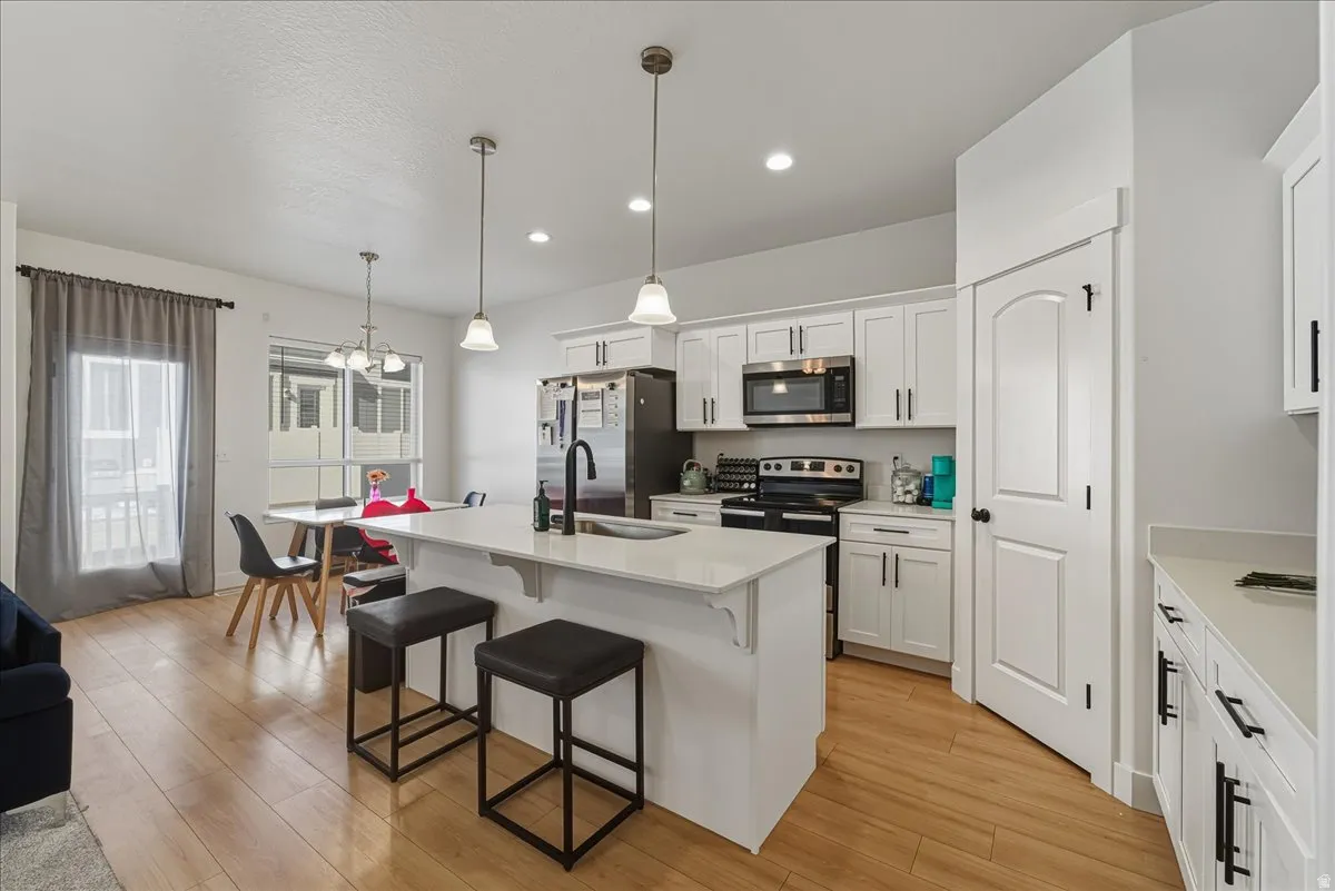 Kitchen featuring a center island with sink, a breakfast bar, white cabinets, stainless steel appliances, and light wood-style floors