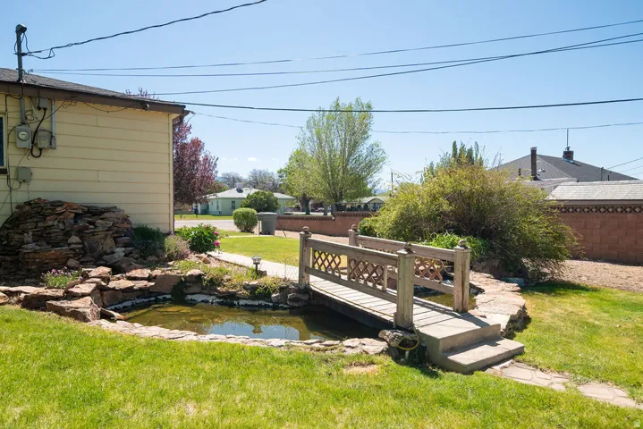Landscaped backyard featuring a decorative wooden footbridge spanning a water feature