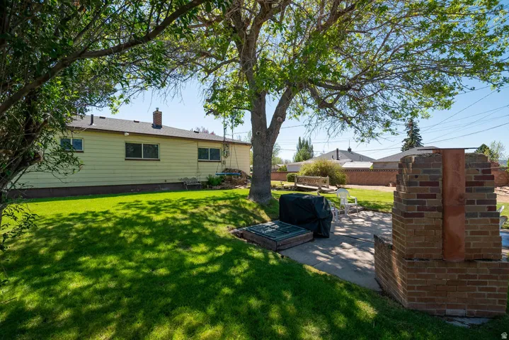 Expansive backyard featuring a manicured lawn, established shade trees, a concrete patio, and a brick outdoor fireplace structure