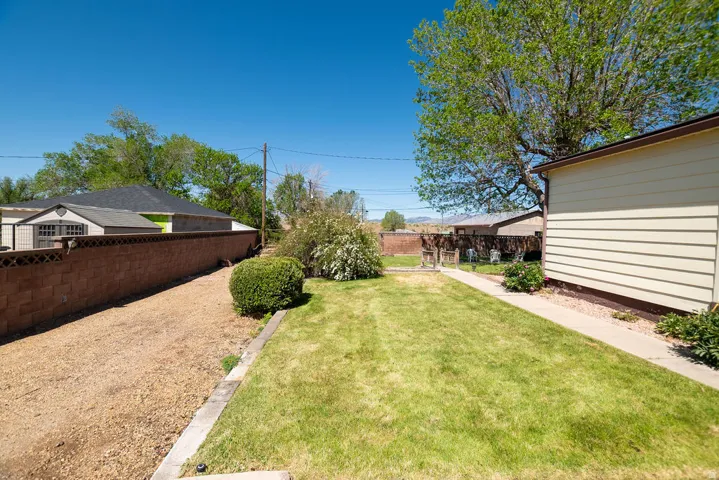 Expansive outdoor space featuring a manicured lawn, a gravel pathway, a partial privacy fence, and mature landscaping