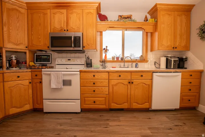 Kitchen featuring white appliances, light countertops, dark wood-style floors, and backsplash