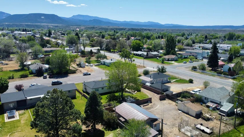 Aerial perspective of a residential area featuring multiple single-story homes, a network of paved streets, abundant mature trees, and distant mountain ranges