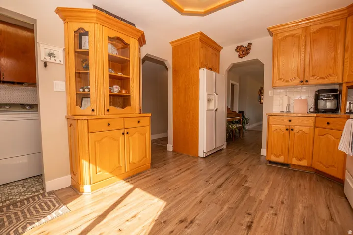 Kitchen with washer / dryer, white refrigerator with ice dispenser, backsplash, light wood-style floors, and arched walkways