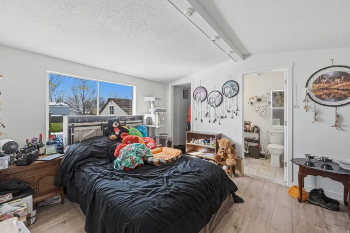 Bedroom with a textured ceiling, light wood-style floors, beam ceiling, and connected bathroom