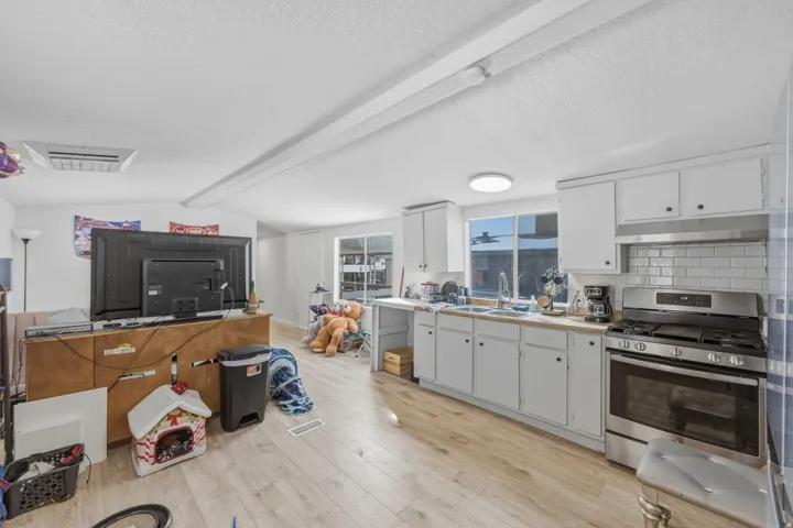 Kitchen featuring stainless steel gas range oven, beamed ceiling, light countertops, light wood-style flooring, and white cabinetry