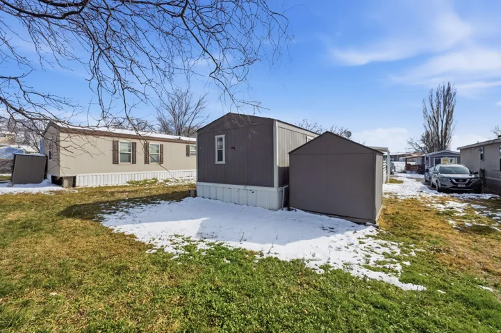Snow covered property with a storage unit and a lawn