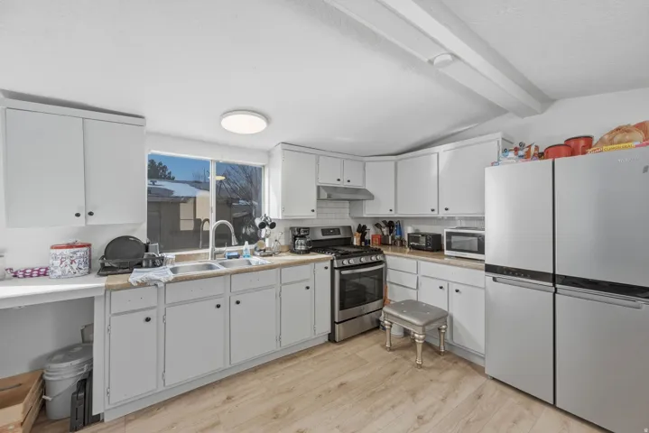 Kitchen featuring stainless steel appliances, light countertops, white cabinetry, decorative backsplash, and beam ceiling