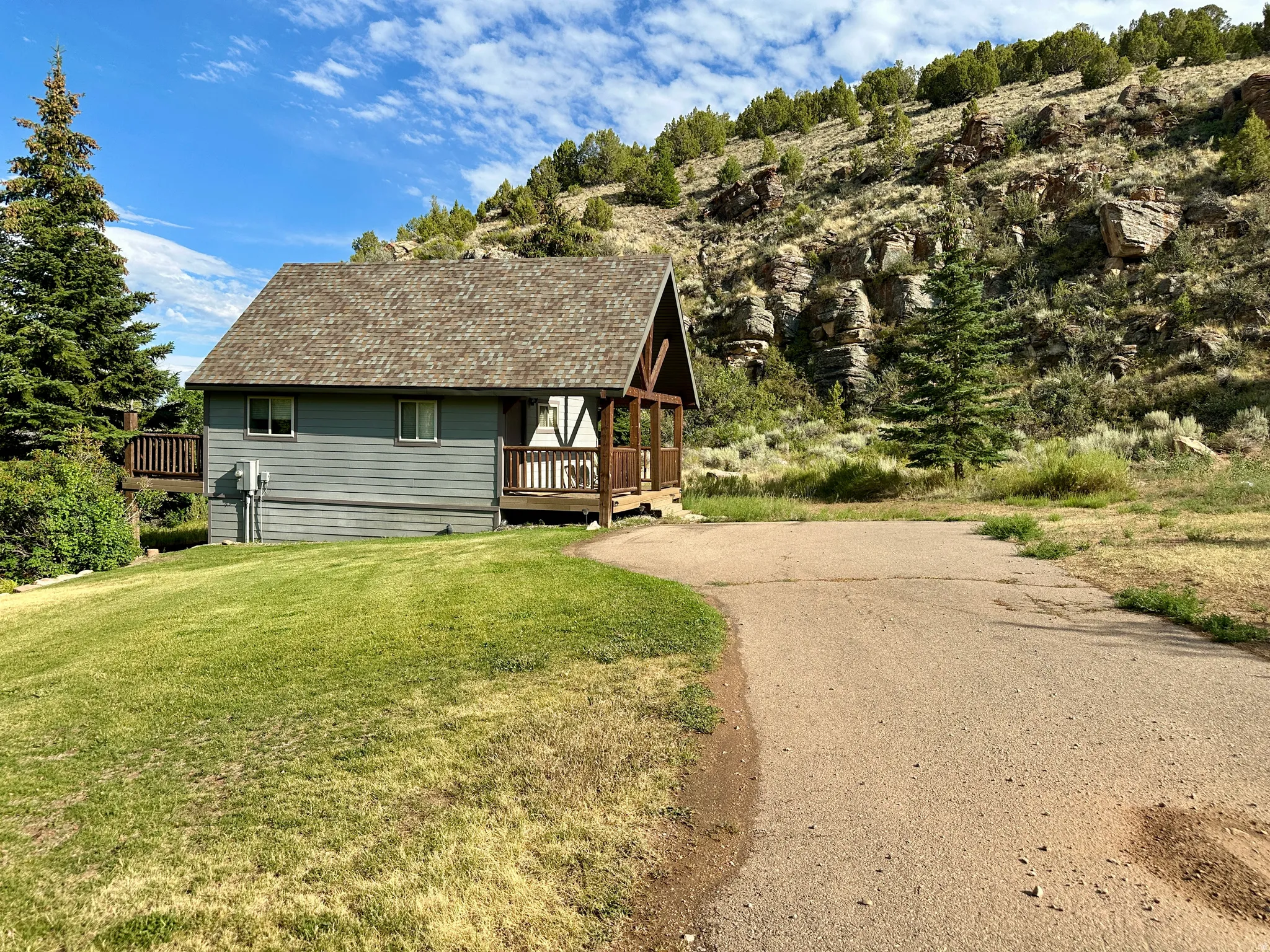 View of front facade with a deck, roof with shingles, a front lawn, and driveway