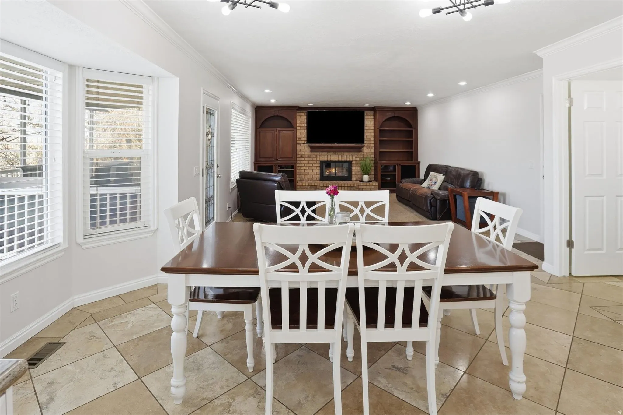 Dining area with a brick fireplace, ornamental molding, light tile patterned floors, and recessed lighting